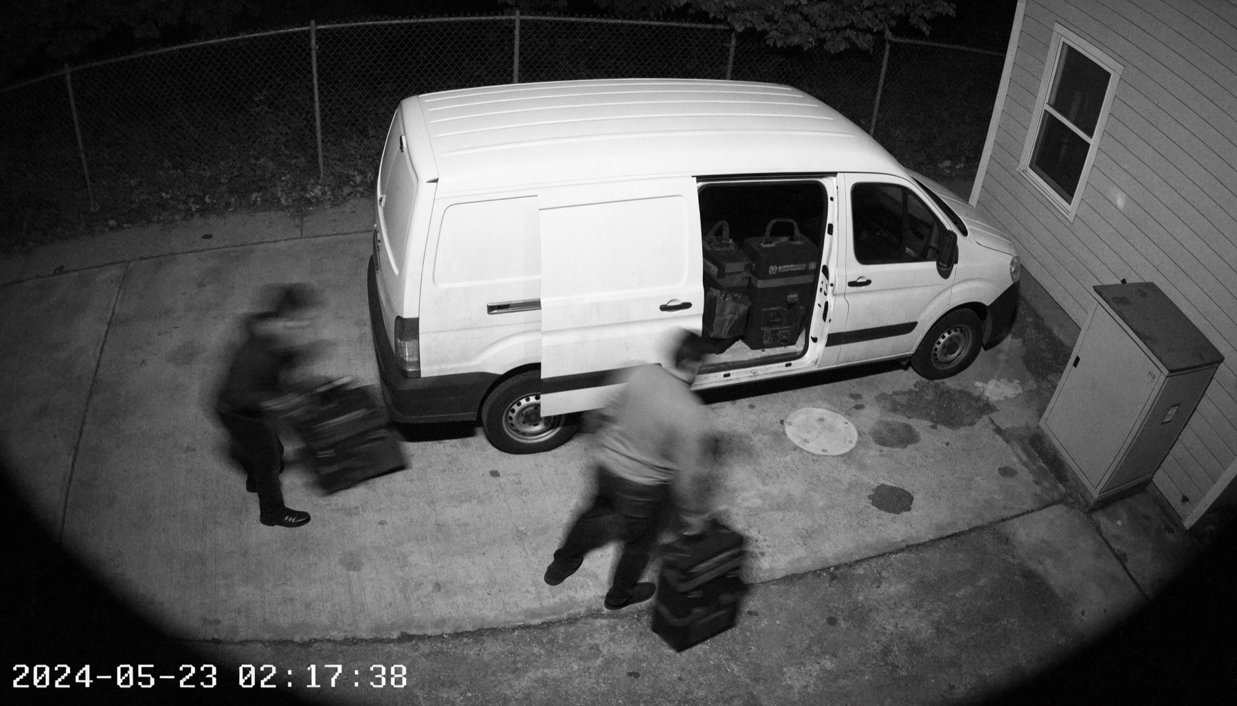 Black-and-white CCTV-style night image of blurry thieves removing tool cases from an open work van.